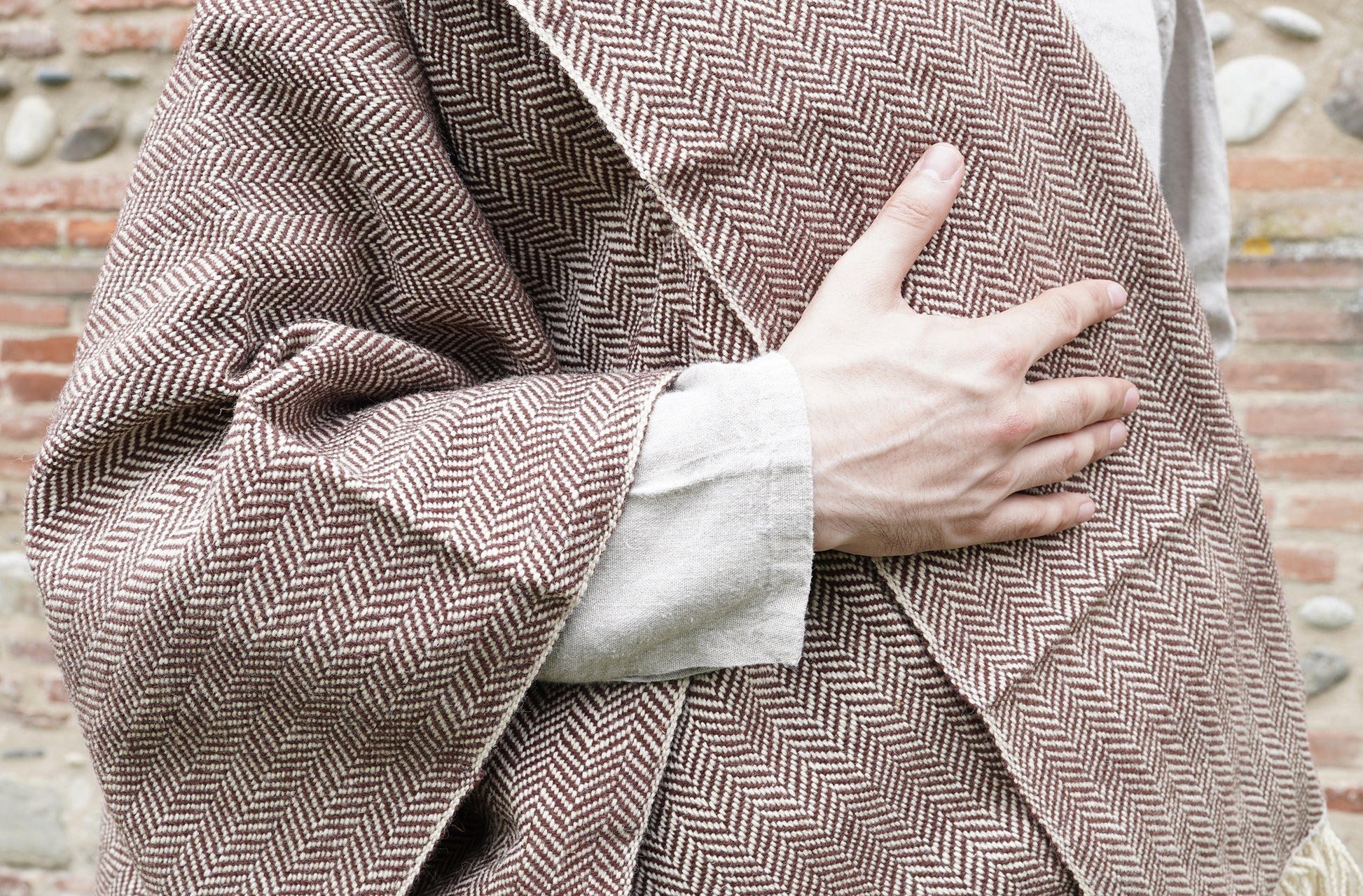 man dressed with Handwoven Herringbone Twill Cloak held by hand closeup 